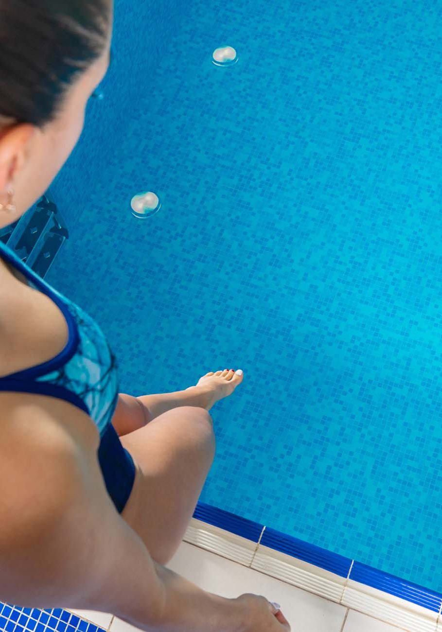 Girl dipping her toe into home swimming pool